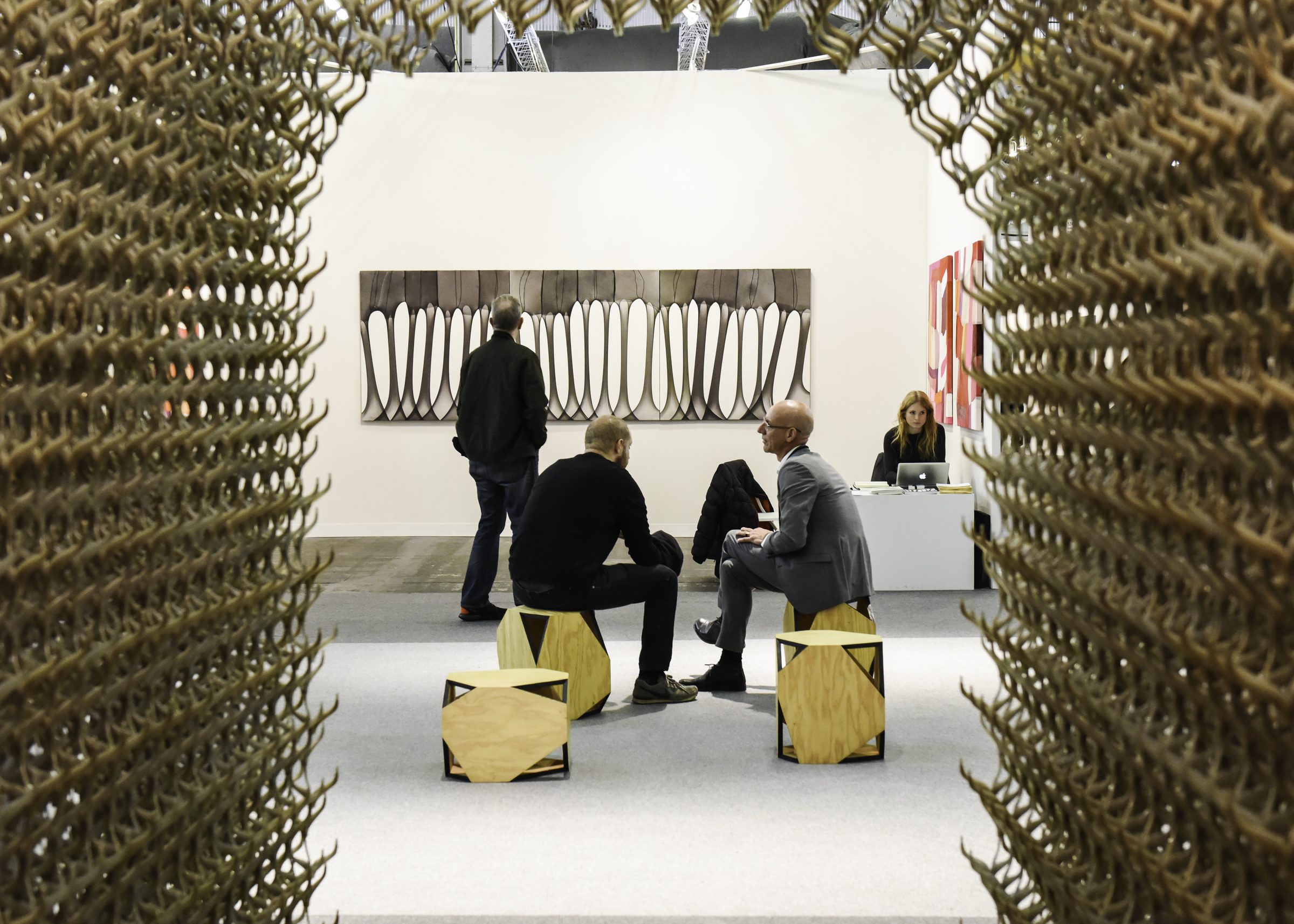 The Armory Show — gallery booth seen through a woven metal screen with sculptural stools